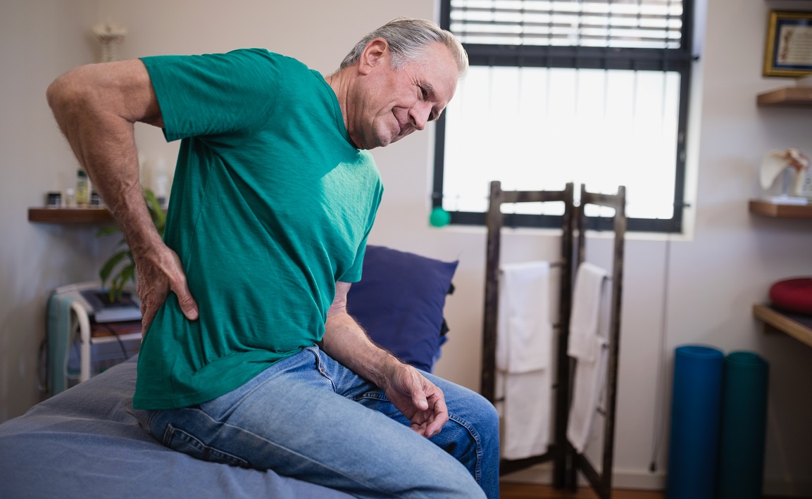 Side View Of Male Patient Suffering From Back Ache While Sitting On Bed
