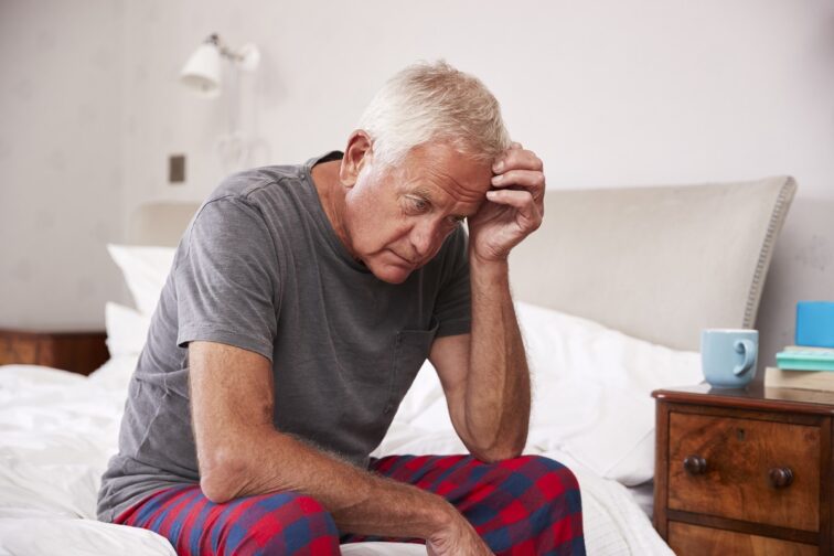 Senior Man Sitting On Bed At Home Suffering From Depression
